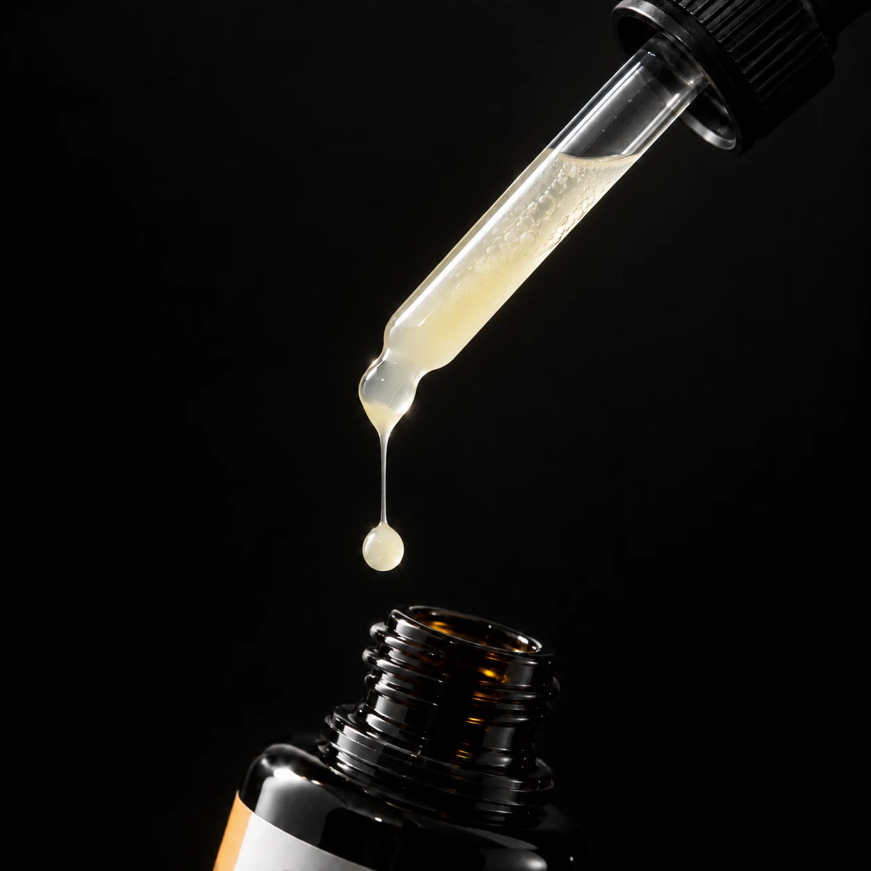 A glass dropper releasing a drop of the Longevity Hybrid Defense Serum above the open bottle, lit against a dark background