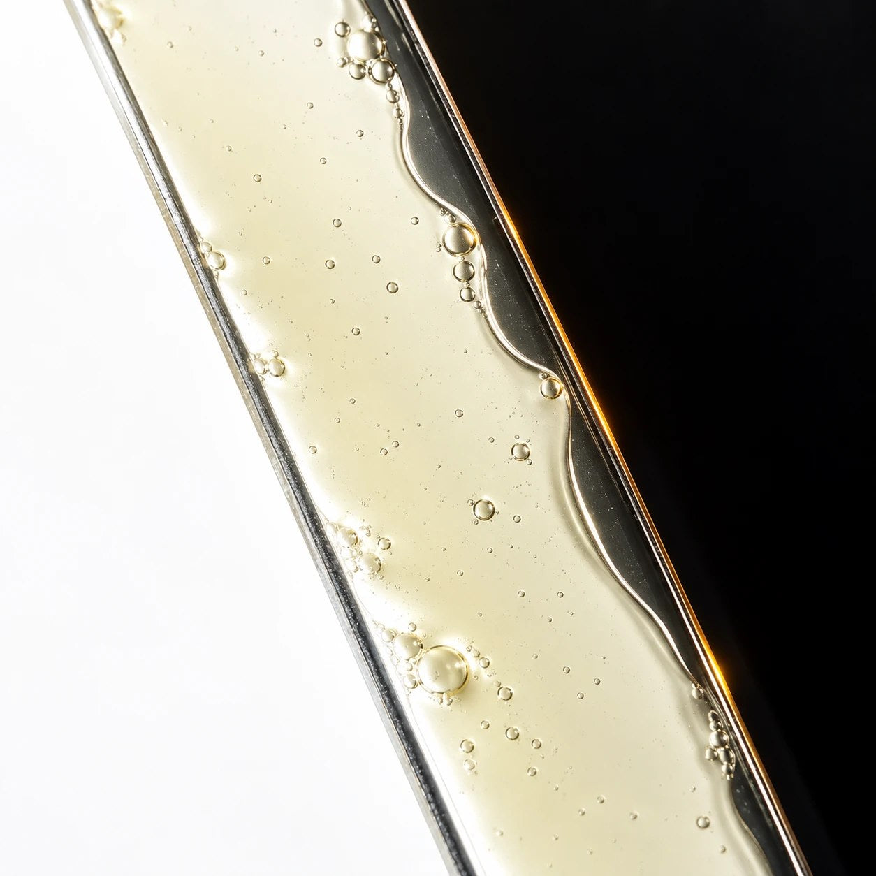 A macro view of the serum, golden and lightly bubbled, against black.